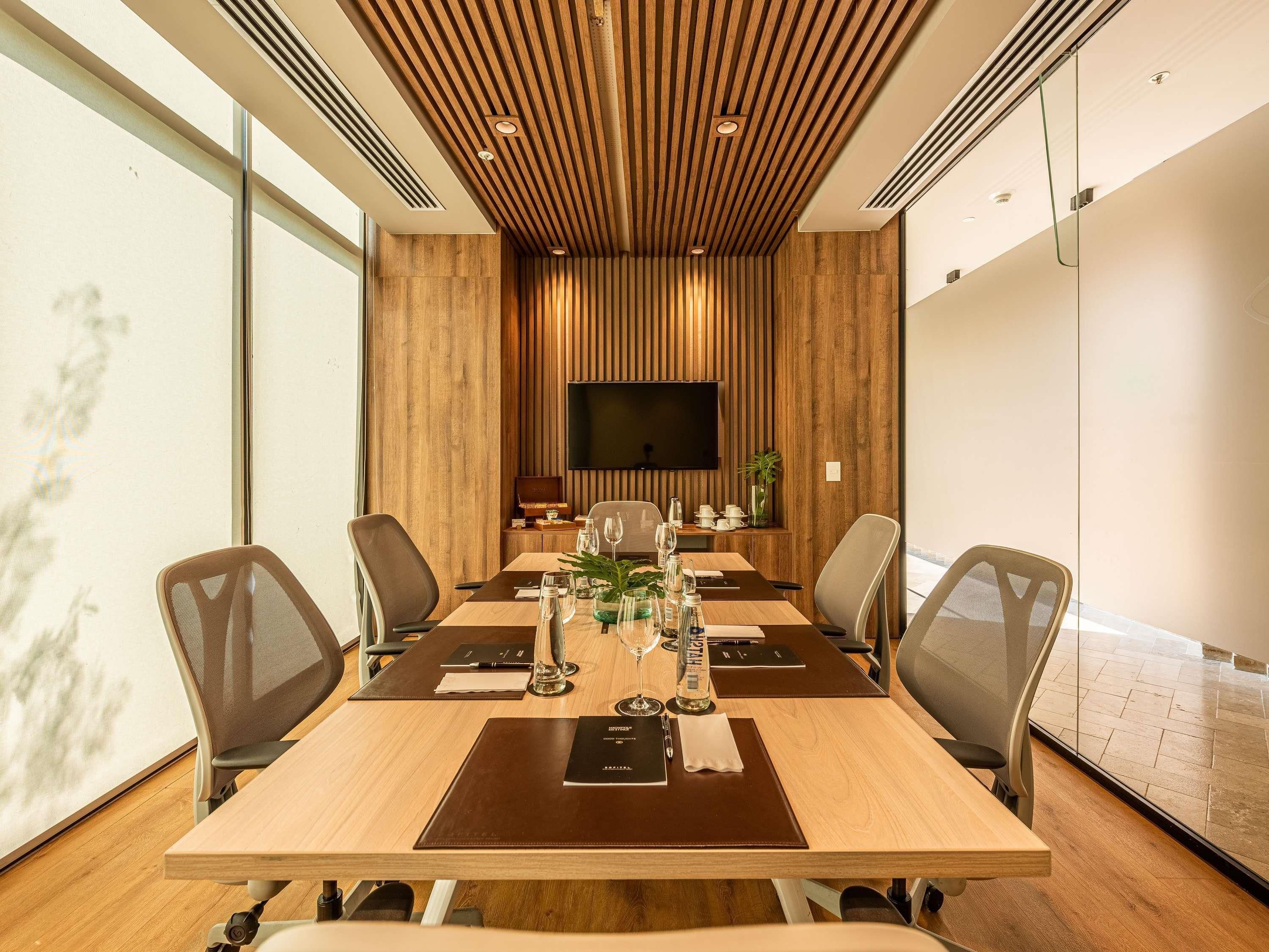 A conference room with a long table, chairs, a flat-screen TV, and a wooden ceiling.