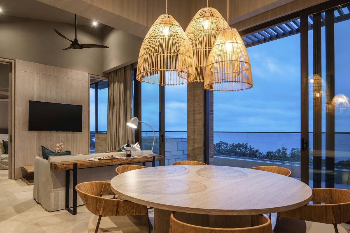 A modern dining area with a round table, wicker chairs, and a large window with a view.