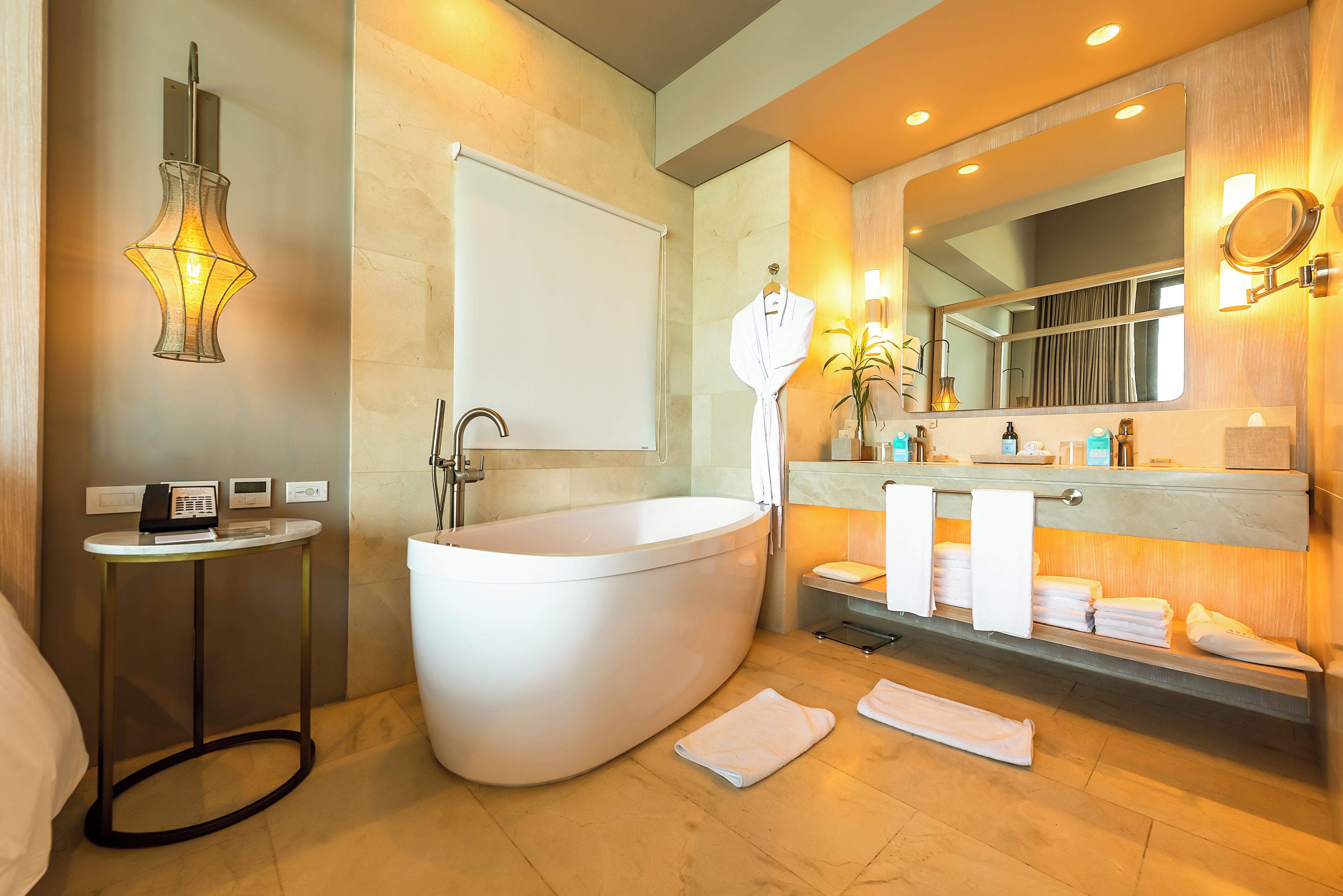 A modern bathroom with a freestanding bathtub, a vanity with a mirror, and a small table with a radio.