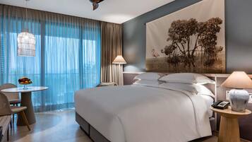 A modern hotel room with a large bed, a desk, a chair, a ceiling fan, and a large window with curtains.