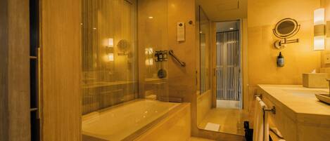 Un baño moderno con ducha envuelta en vidrio, una bañera grande y un tocador con espejo e iluminación.