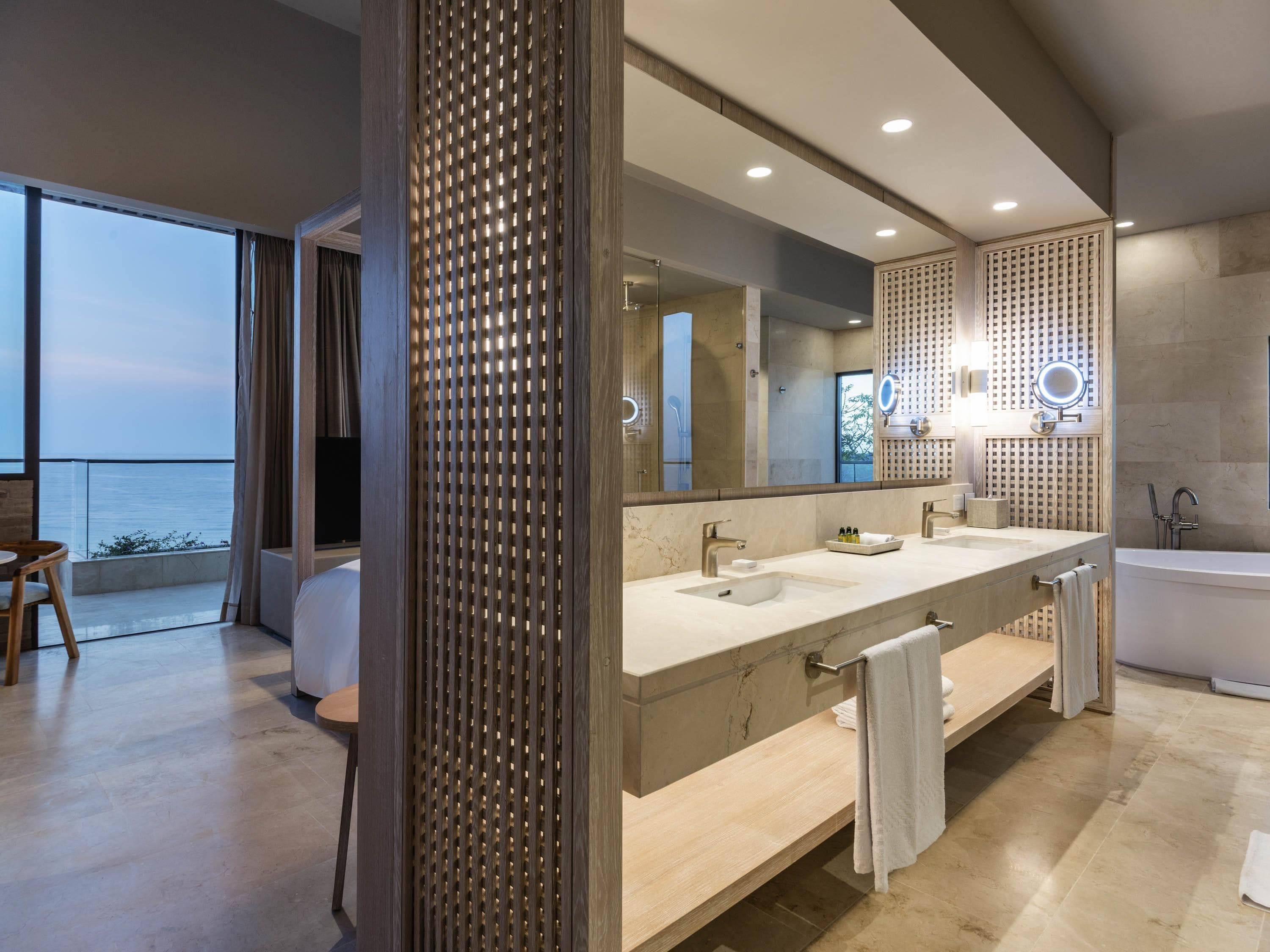 A modern bathroom with a large mirror, dual sinks, and a bathtub.
