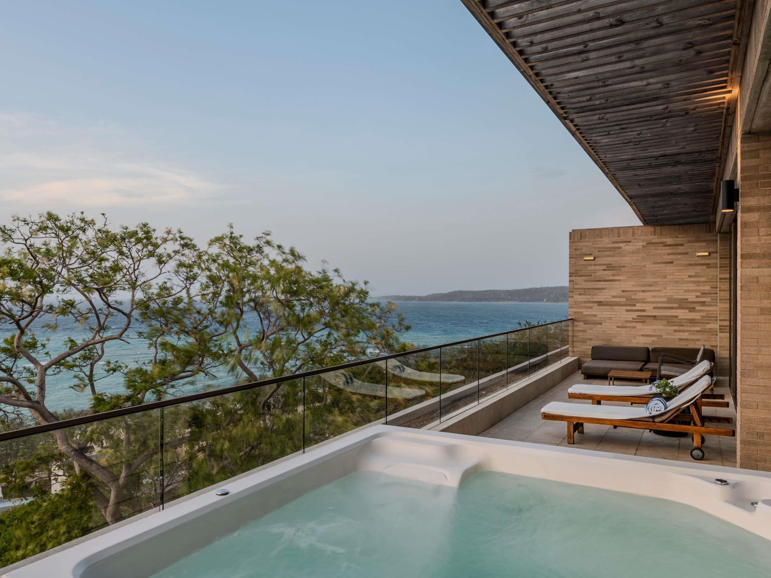 A modern outdoor area with a hot tub, lounge chairs, and a view of the sea.