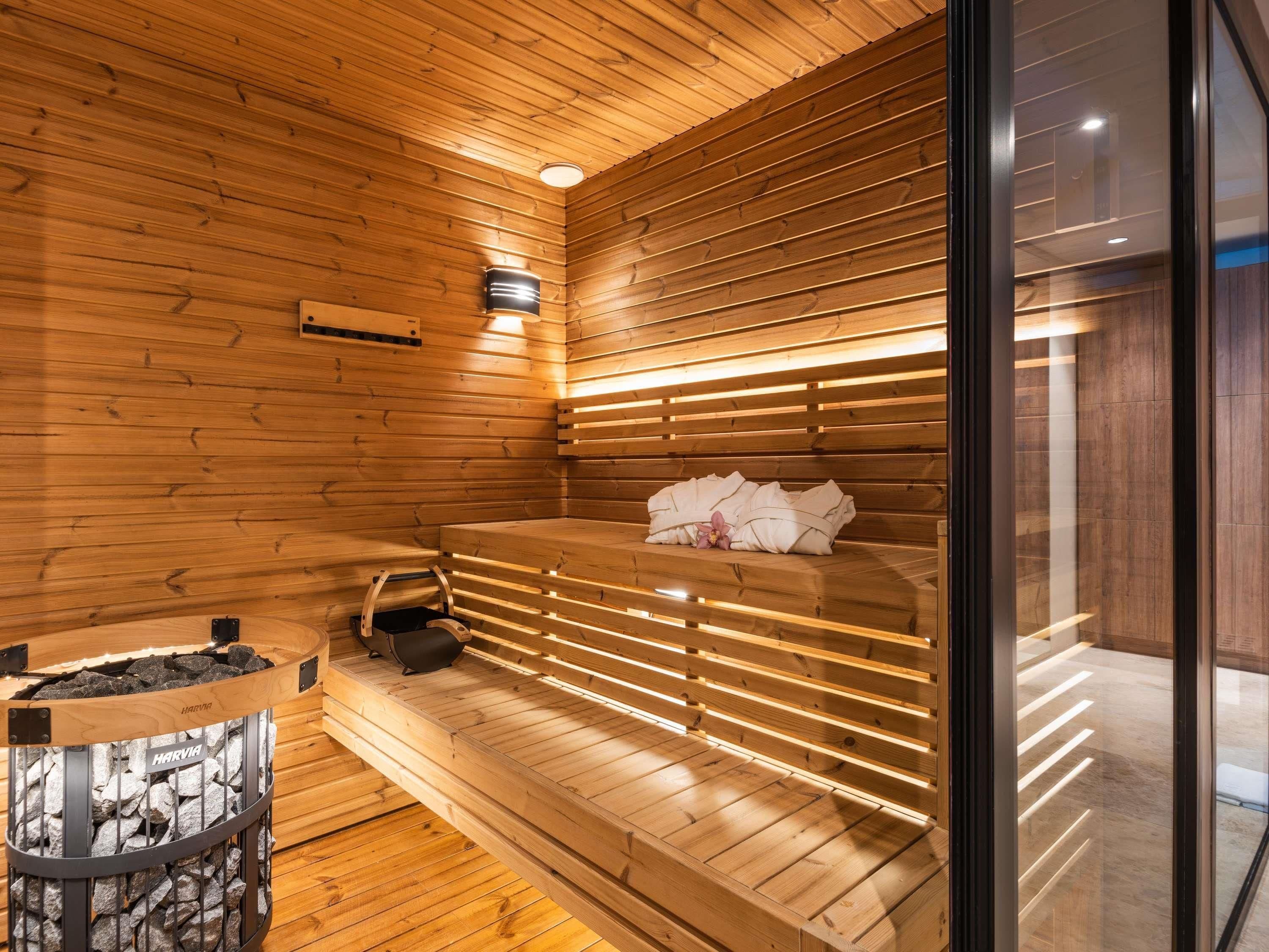 Una sauna con listones de madera, un banco, un calentador de banco y un recipiente de piedra.