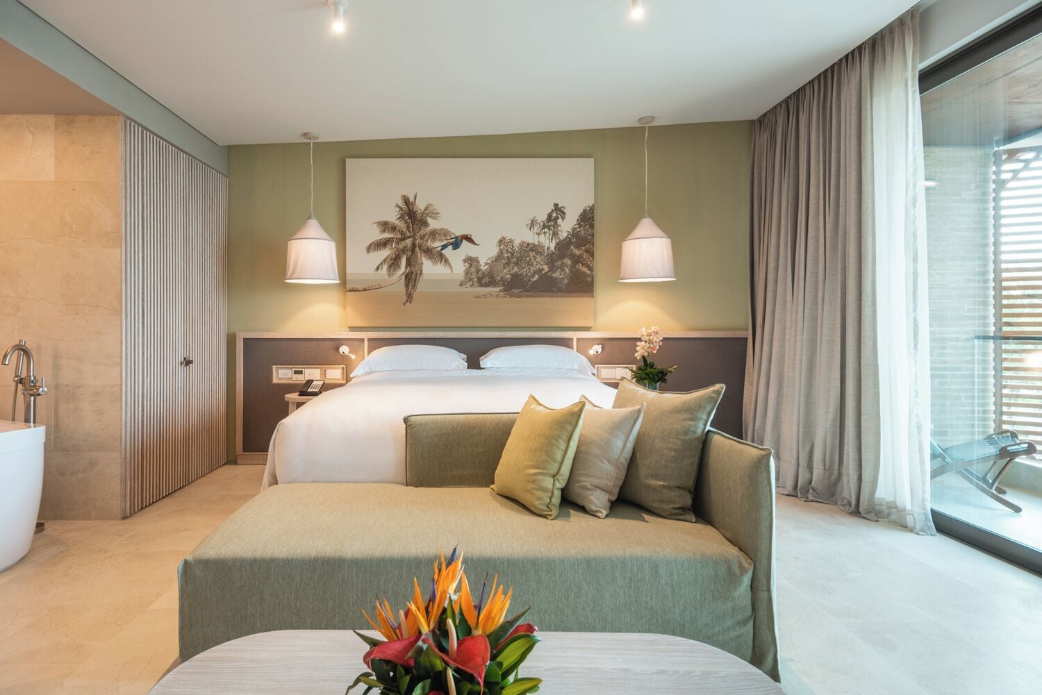 Habitación de hotel moderna con una cama grande, un sofá, un baño y un ventanal con cortinas.