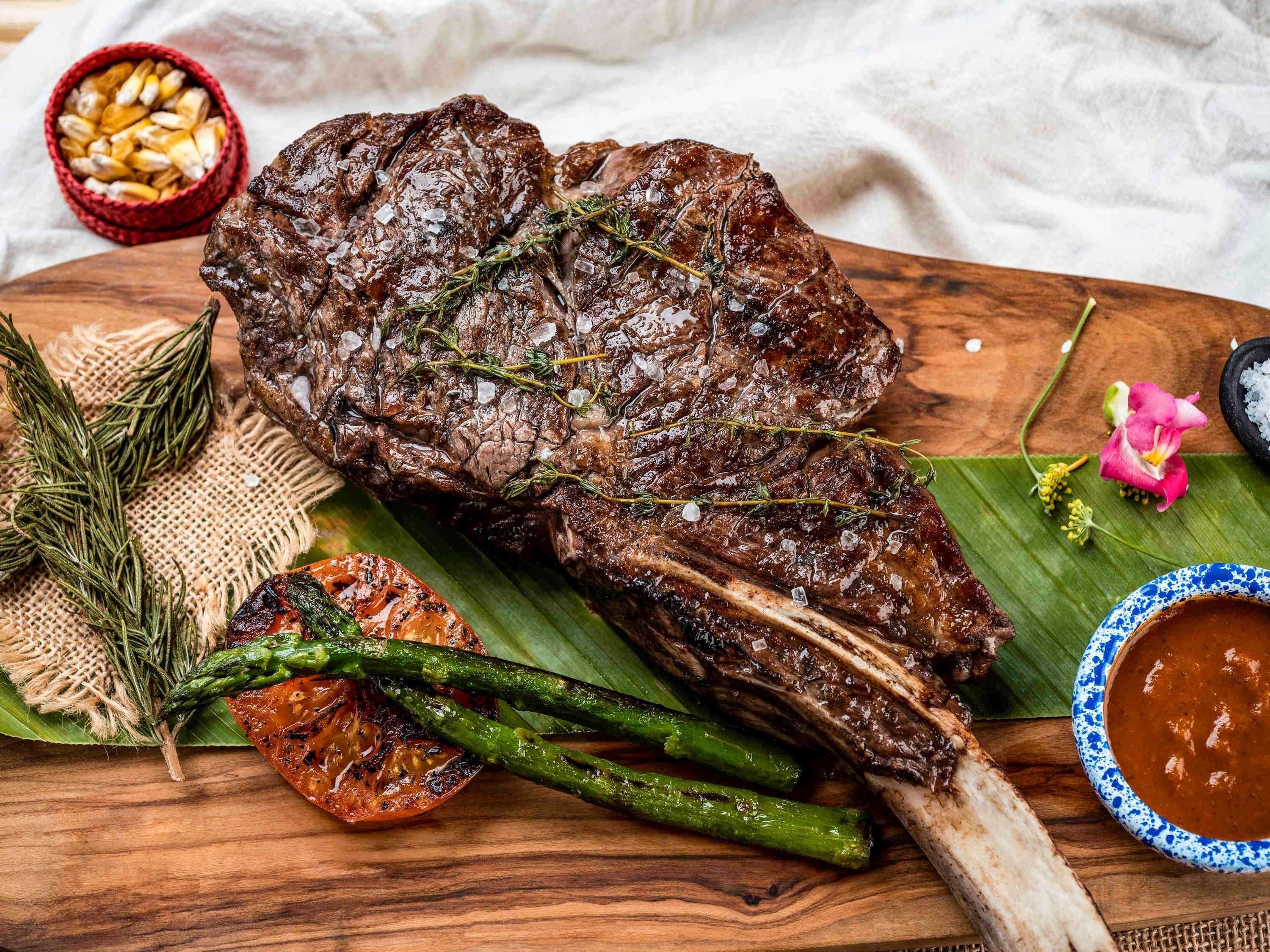 Bistec con espárragos y salsa acompañada en una tabla de madera.