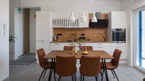 A modern kitchen with white cabinets, a wooden countertop, and a built-in oven. There are four brown chairs around a wooden dining table.