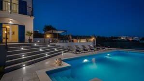 A modern pool area with steps leading to a pool, lounge chairs, and a building with a balcony.