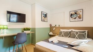 Un dormitorio con cama, escritorio, silla, televisor y obras de arte en las paredes.
