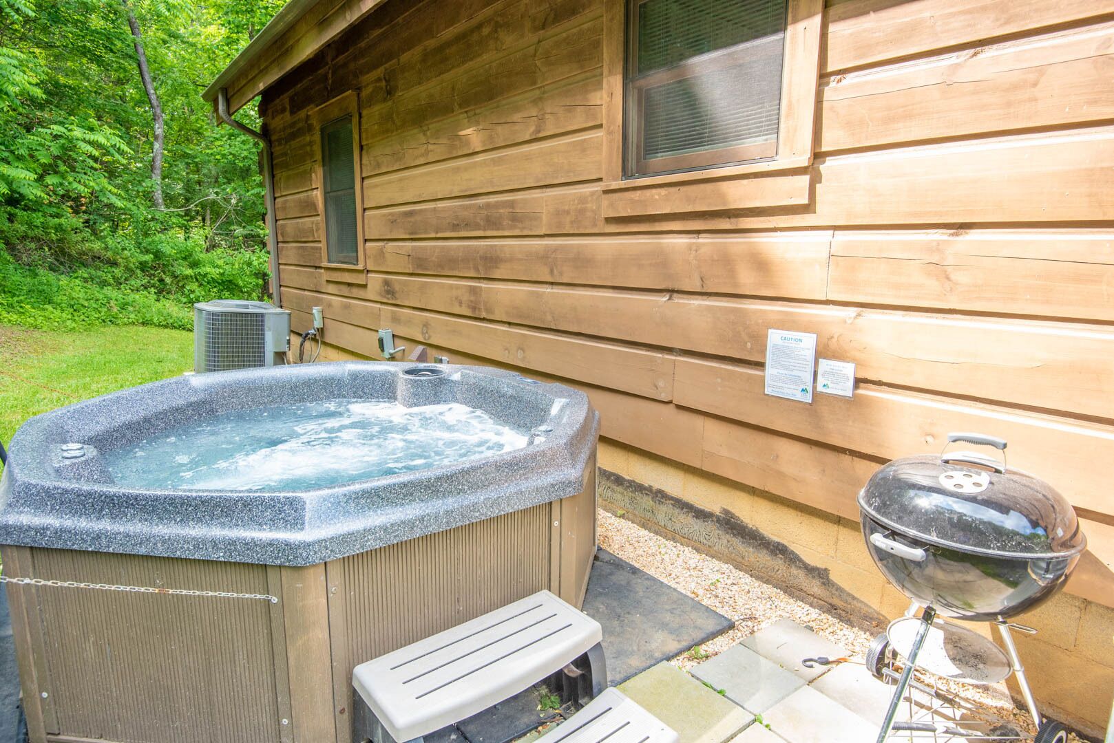 A wooden cabin with a hot tub, a barbecue grill, and a bench.