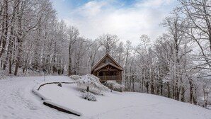 Una cabaña de madera rodeada de árboles cubiertos de nieve, bajo un cielo despejado.