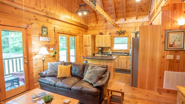 Un interior acogedor de cabaña con sofá de cuero, piso de madera, una zona de cocina y una mesa de comedor.