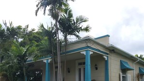 A two-story house with a porch, surrounded by lush greenery and palm trees.