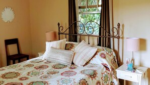 A bedroom with a bed, bedside table, chair, window with curtains, and an air conditioning unit.