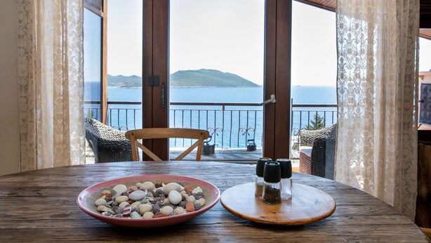 A wooden table with a bowl of snacks and salt and pepper shakers, a chair, and a view of the sea through a glass door.