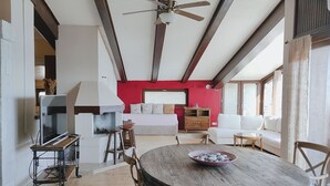 A spacious living area with a wooden dining table, a ceiling fan, and a red accent wall.