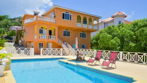 Un grand bâtiment à deux étages, doté d’une piscine, d’une clôture blanche et de plusieurs chaises longues.