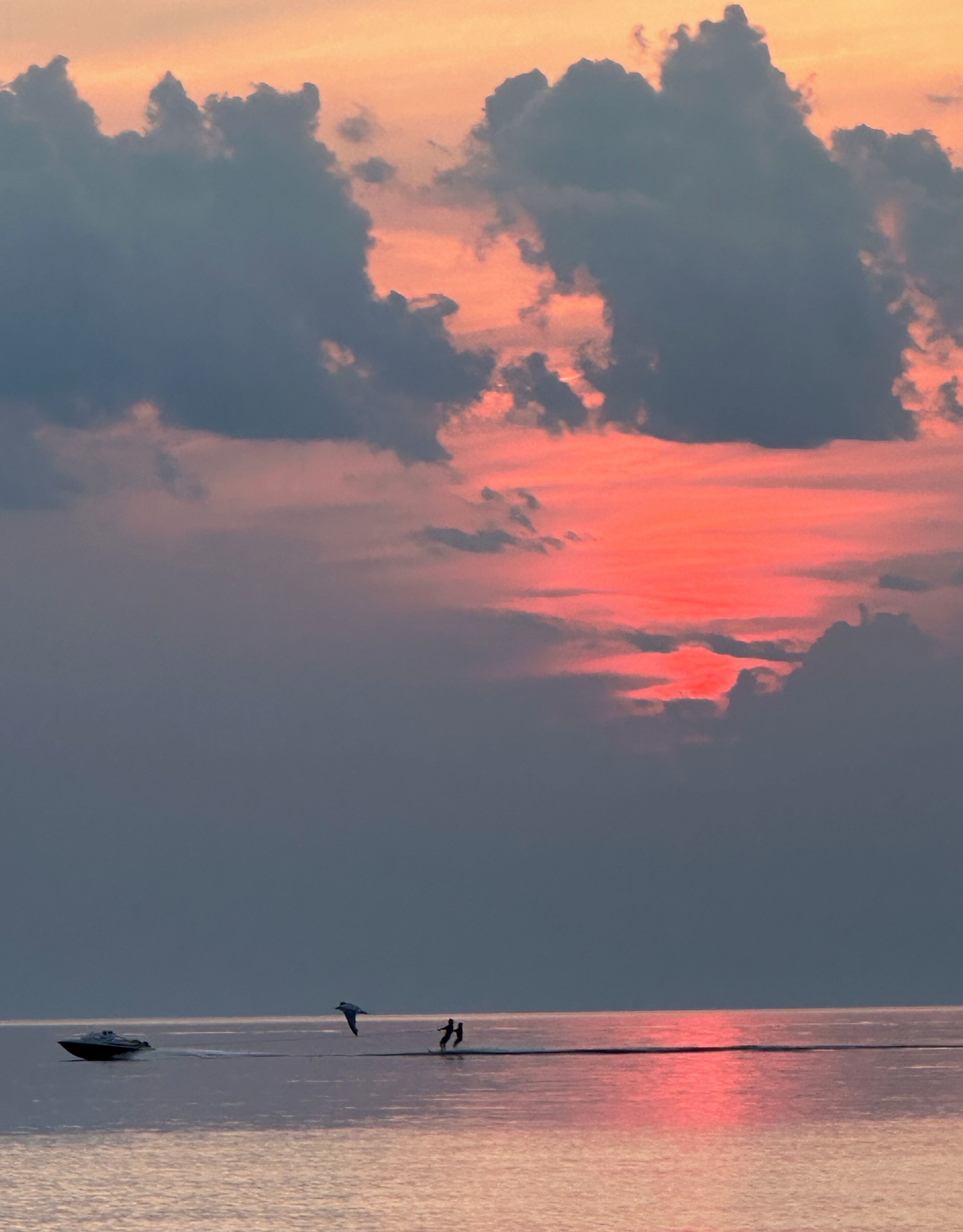 A sunset over a body of water with a boat and two people on the shore.