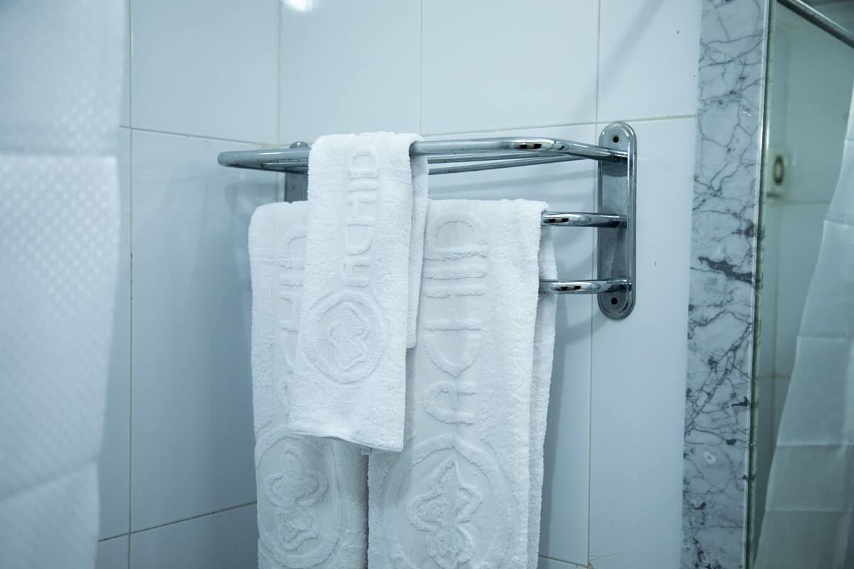 A bathroom with white tiled walls, a marble accent wall, and a towel rack with two white towels.