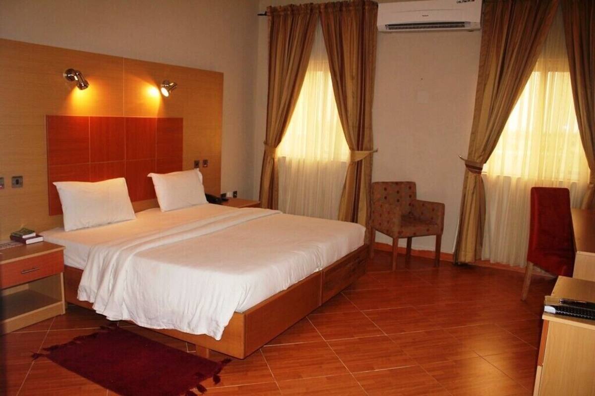 A hotel room with a wooden bed, two bedside tables, a chair, and a desk with a computer.
