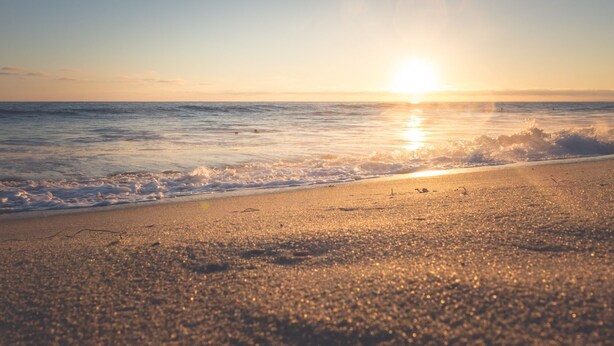 Een strand met de zon die in de oceaan ondergaat, wat een rustgevende sfeer creëert.