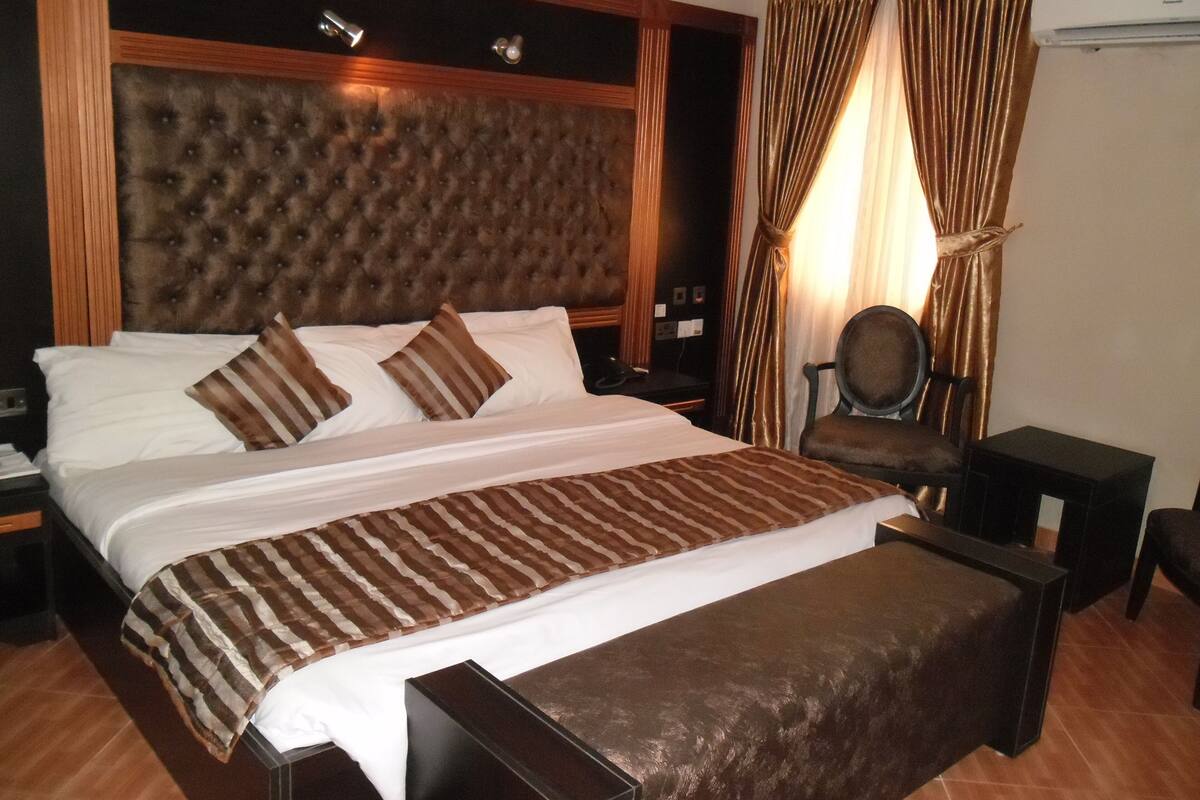 A large bed with a tufted headboard, a bedside table, a chair, and a small table.