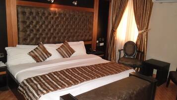 A large bed with a tufted headboard, a bedside table, a chair, and a small table.