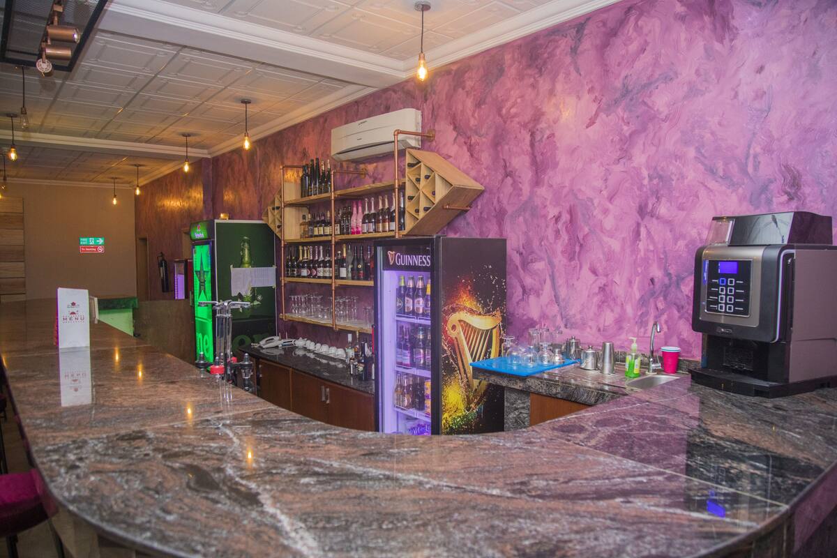 A bar area with a marble countertop, shelves with liquor bottles, a refrigerator, and a digital payment terminal.