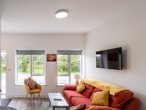 Una sala de estar moderna con un sofá rojo, un sillón amarillo y un televisor de pantalla plana montado en la pared.