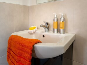 Un lavabo de salle de bain avec un receveur blanc, un robinet argenté et deux flacons de savon liquide et de lotion.