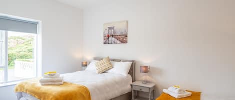 Una camera d'hotel moderna con un letto grande, un letto più piccolo, un comodino, una lampada e un quadro raffigurante un ponte.