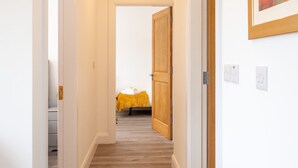 Um corredor com uma porta de madeira que dá para um quarto com uma cama coberta por um cobertor amarelo.