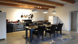 A modern kitchen with a dining area, featuring a large table, chairs, hanging lights, and a refrigerator.