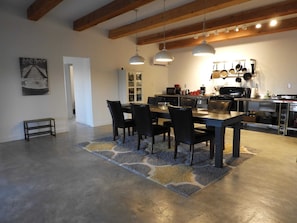 A modern kitchen with a dining area, featuring a large table, chairs, pendant lights, and a visible refrigerator.