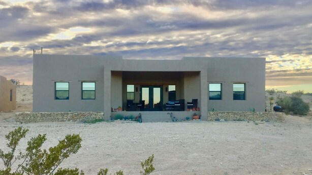 A modern two-story building with a flat roof, large windows, and a covered entrance area with outdoor seating.