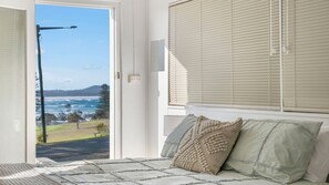 A bedroom with a bed, pillows, a view of the ocean, and a door leading outside.