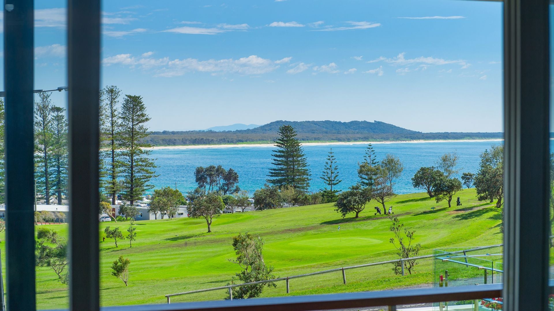A view of a coastal golf course with a beach and ocean in the background.