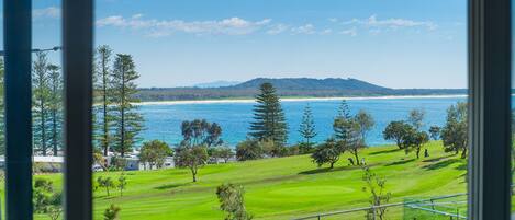 A view of a coastal golf course with a beach and ocean in the background.
