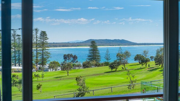 A view of a coastal golf course with a beach and ocean in the background.