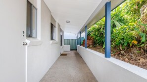 A narrow corridor with white walls, a concrete floor, and a green fence on one side.