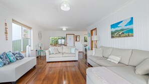 A spacious living room with a large sofa, a smaller sofa, and a coffee table. There is a painting on the wall and a window providing natural light.
