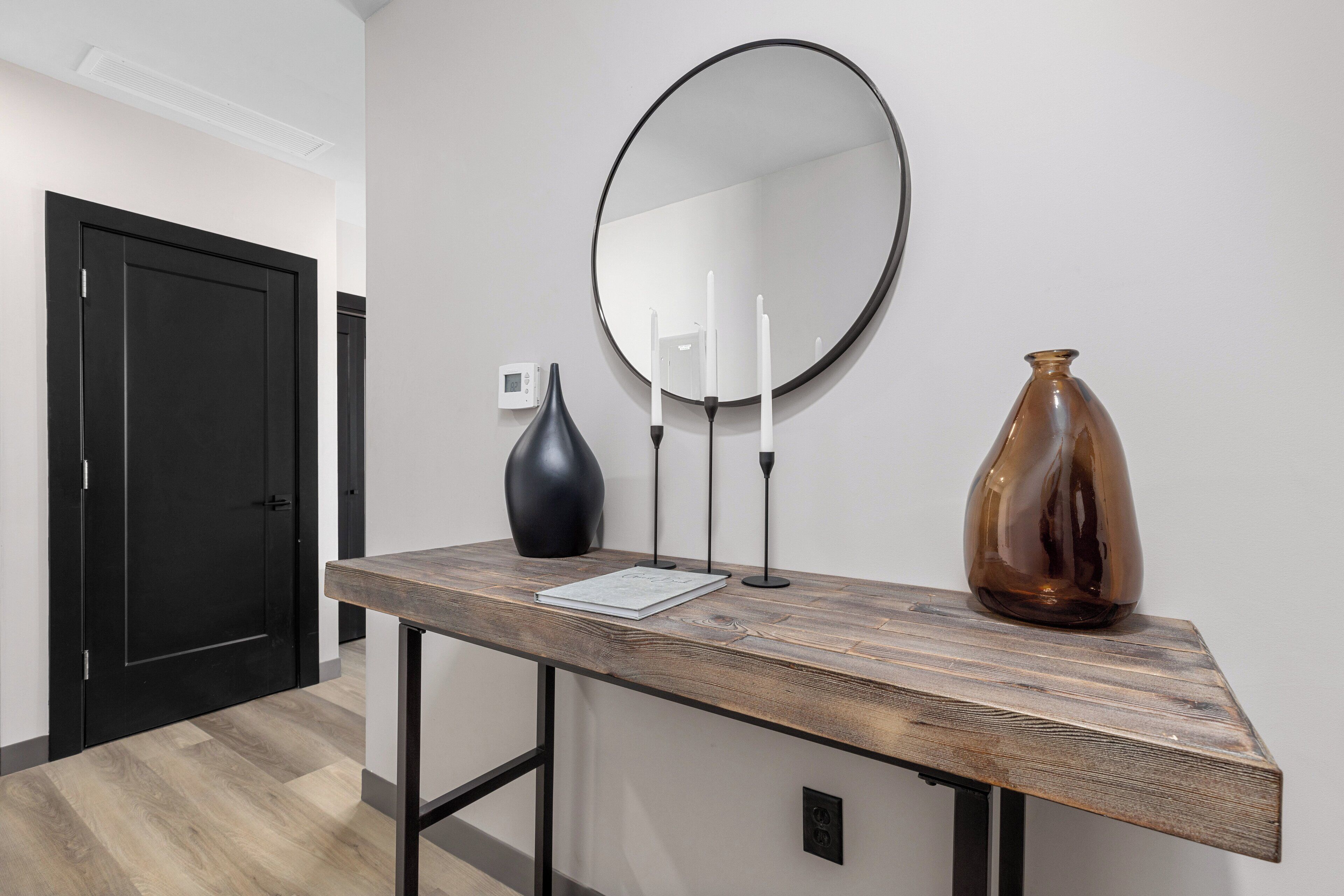 A modern interior with a wooden console table, a round mirror, a vase, and a book.