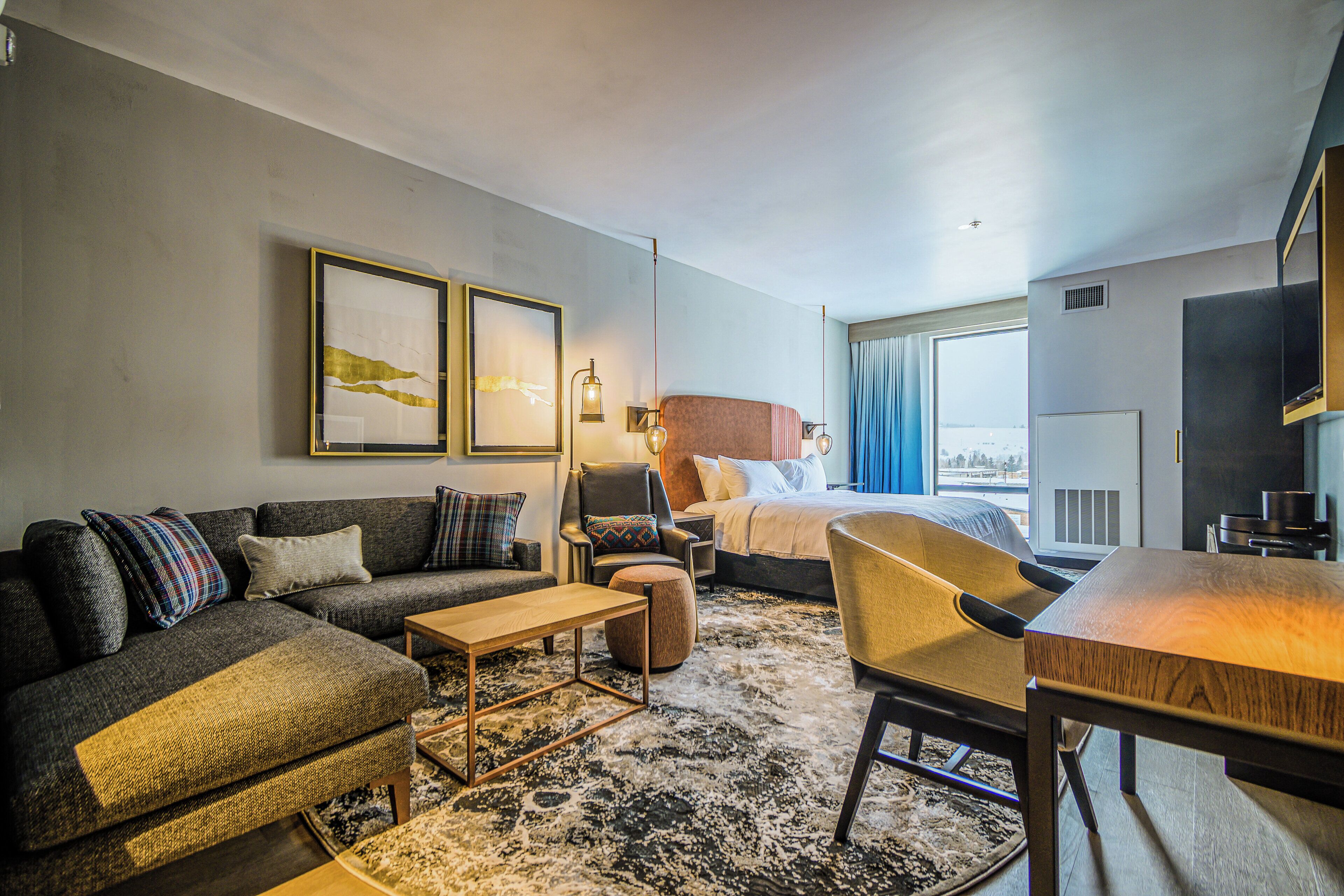 A modern hotel room with a sofa, armchair, bed, and a dining table.