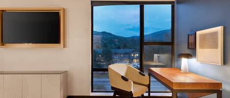 A modern room with a large window, a desk, a chair, and a TV.