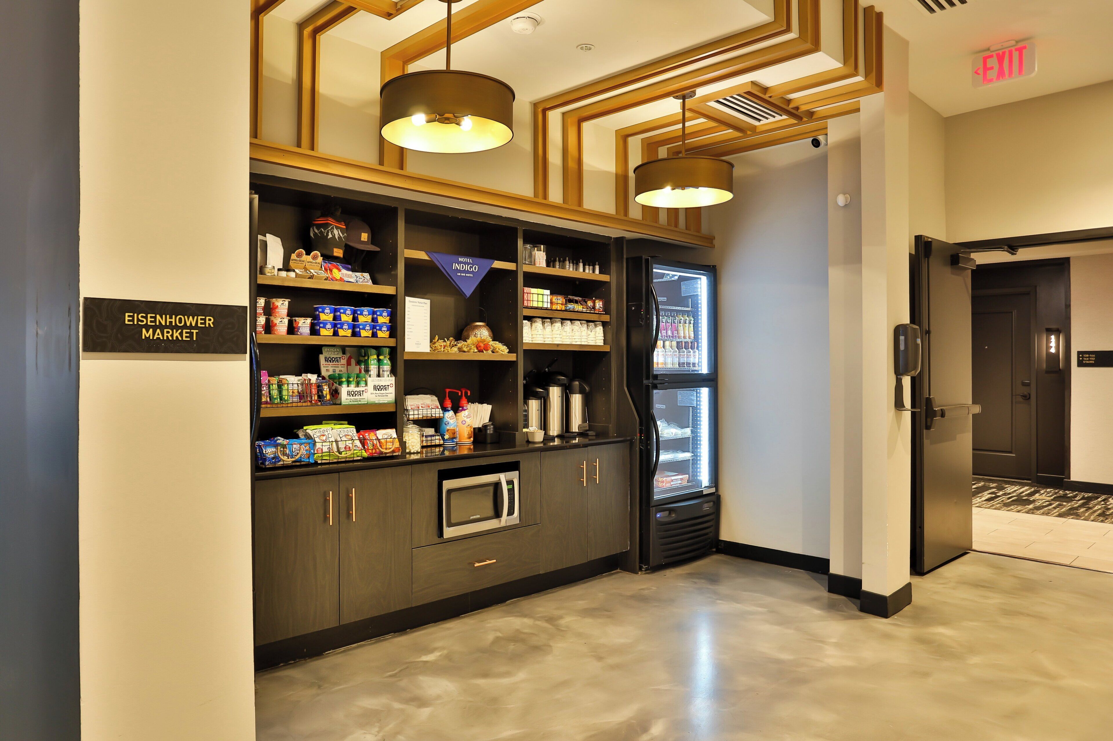 A hotel market area with a refrigerator, shelves stocked with snacks, and a sign indicating the location.