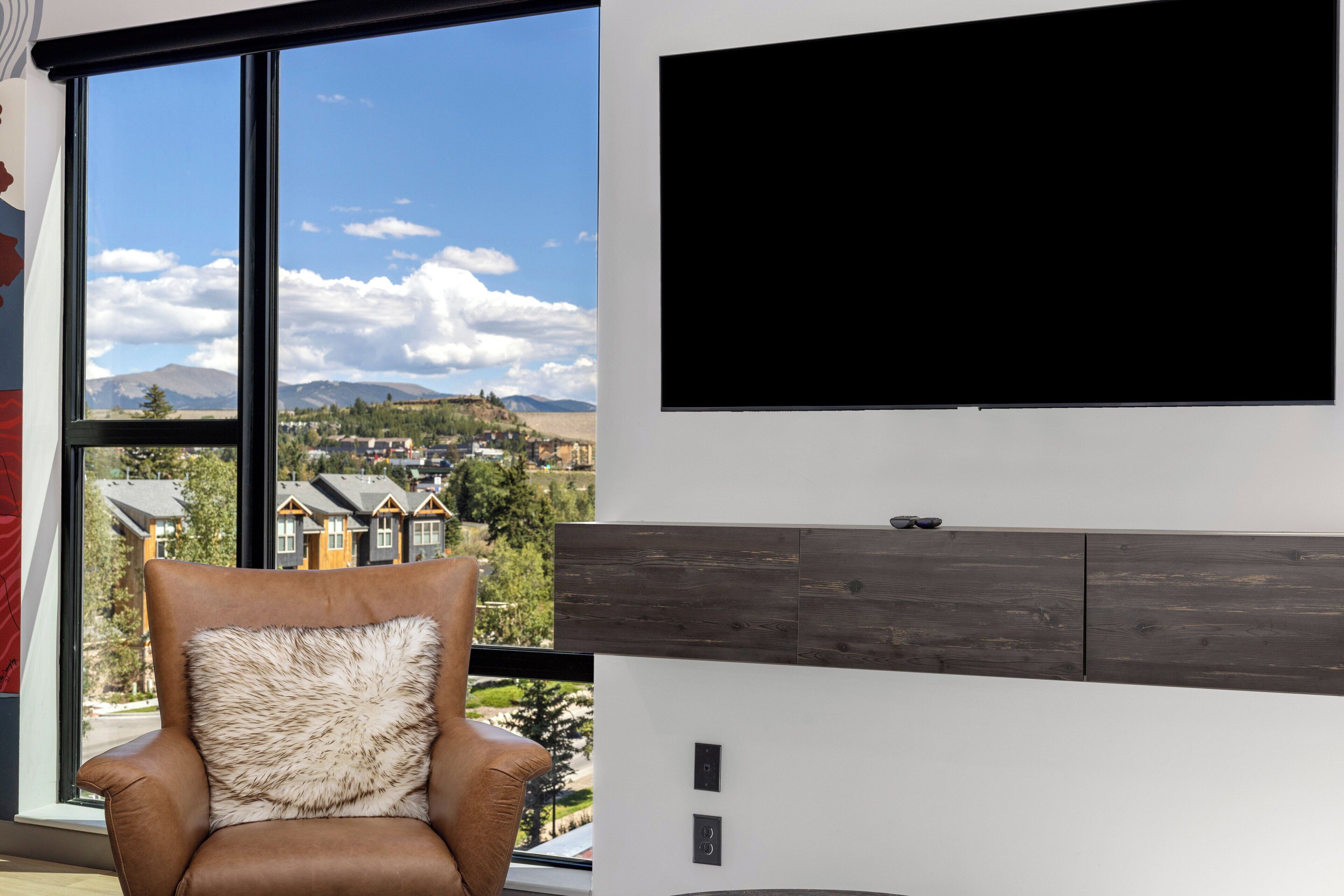 Una stanza moderna con un'ampia finestra, una TV a parete e una poltrona in pelle marrone con un cuscino soffice.