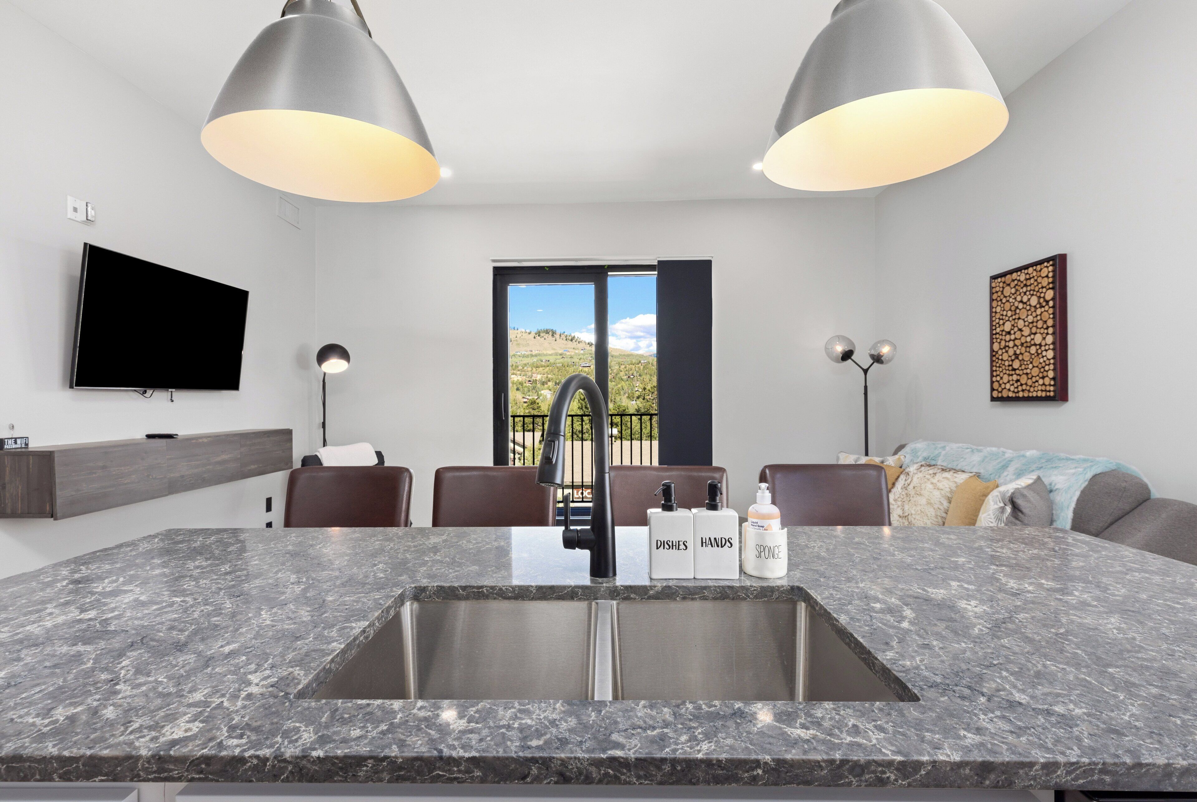 A modern kitchen with a granite countertop, stainless steel sink, and pendant lighting.