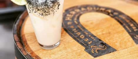 Un vaso de una bebida cremosa con una cuña de lima y un poco de polvo negro encima, sobre un barril de madera con un logotipo.