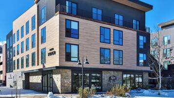 A modern multi-story building with a mix of wood and stone facade, featuring a restaurant named "Kitu" and a sign for "Tacos & Carne."