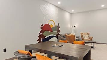 Ein moderner Essbereich mit einem dunklen Holztisch, grau gepolsterten Stühlen und orangefarbenen Kissen.